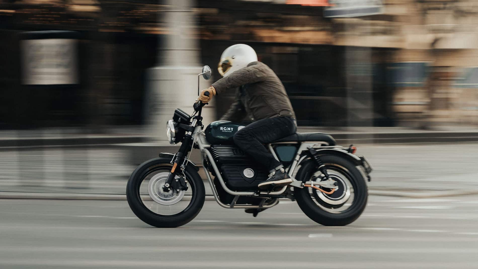 RGNT Scrambler electric motorcycle riding on city streets. 