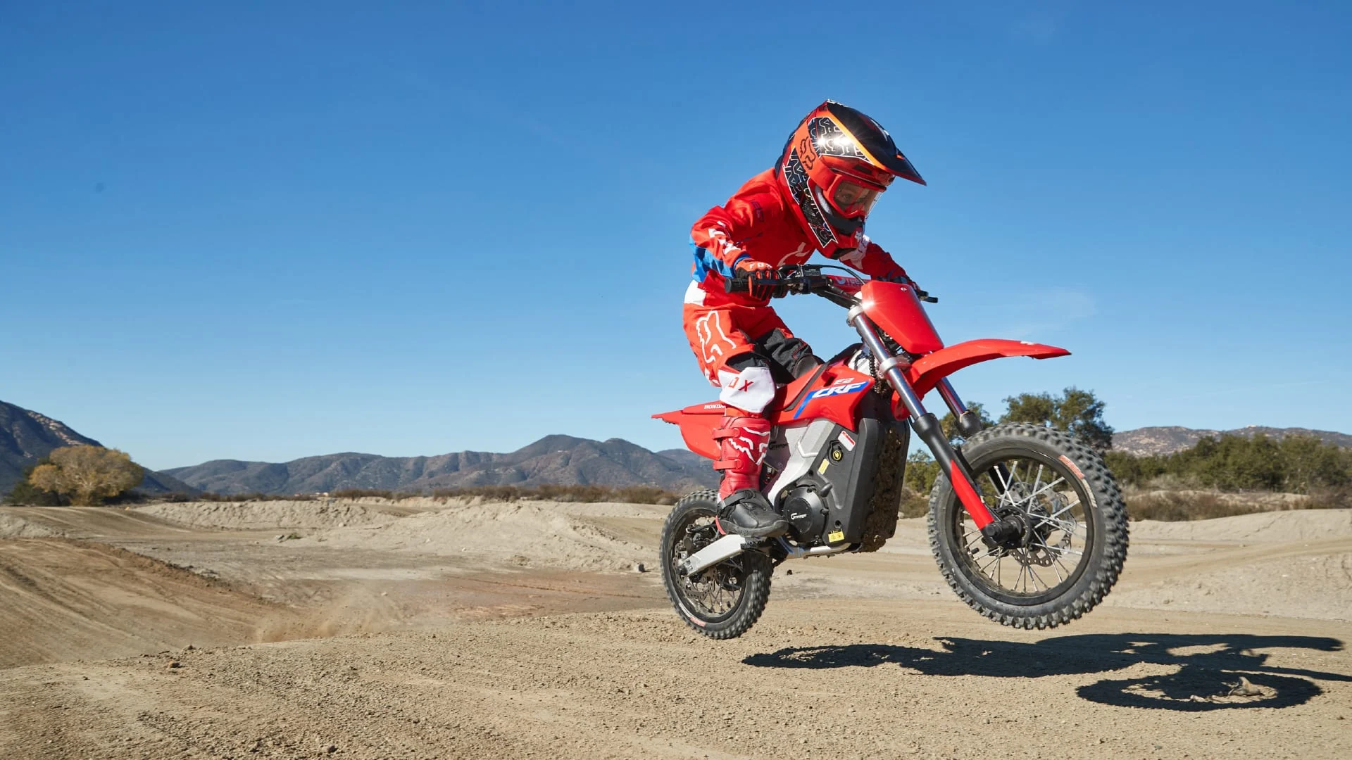 Youth jumping a Honda CRF-E2 motorcycle in the desert.