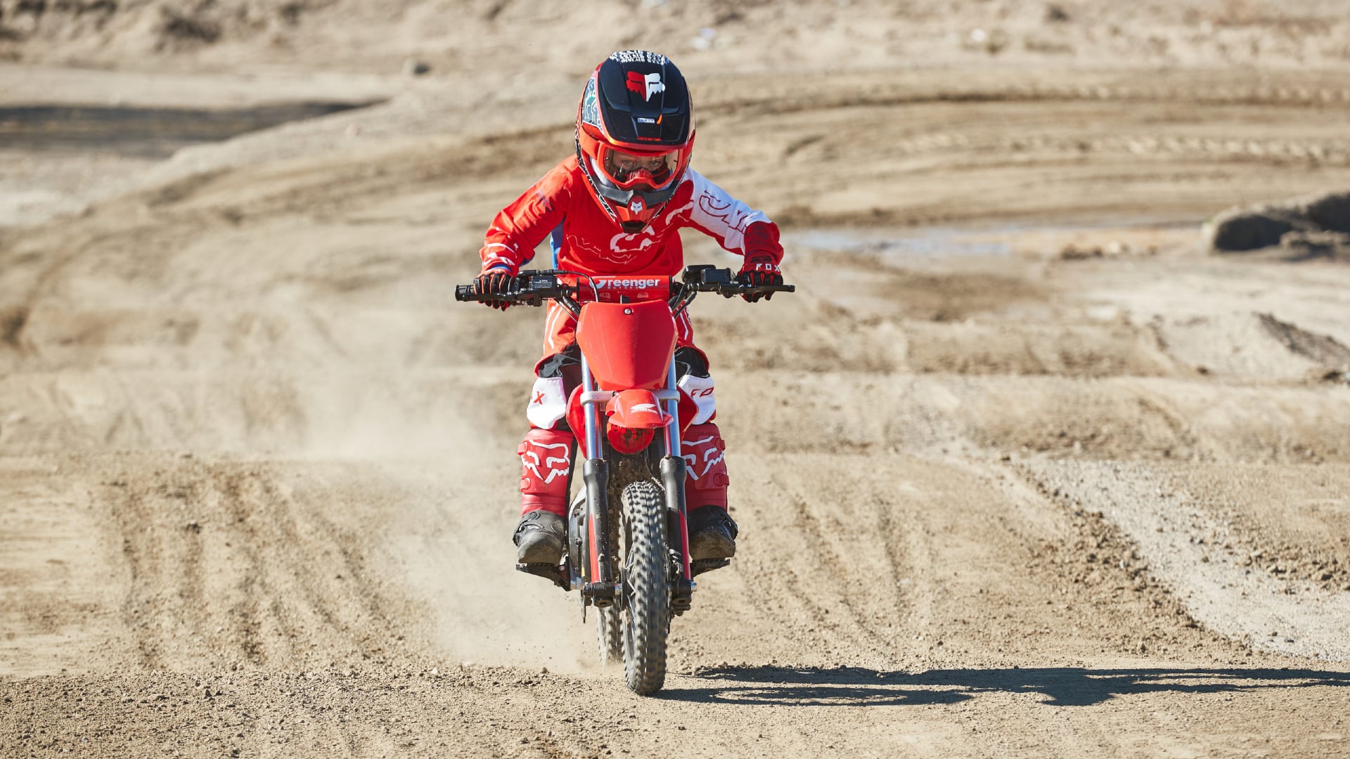 A kids electric dirt bike going through whoops on a race track.